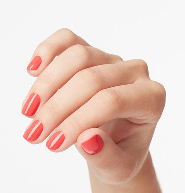 Model's hand wears a coral nail polish shade