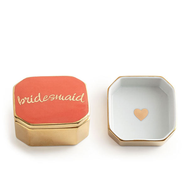 Square gold box with beveled corners, white interior with gold heart decal, and coral lid printed with "Bridesmaid" in gold script lettering