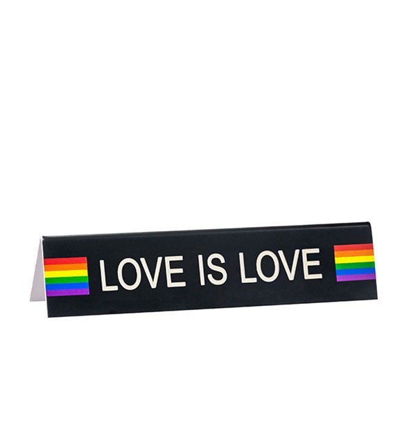 Rectangular black sign says, "Love Is Love" in white lettering flanked by rainbow graphics