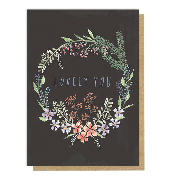 Dark grey greeting card with colorful floral wrath illustration says, "Lovely You" in the center