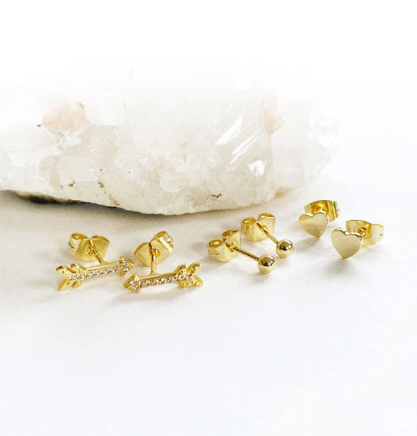 Jewel-encrusted arrow, gold heart, and gold ball stud earrings closeup