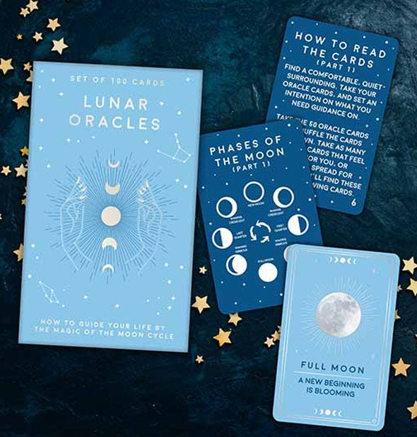 Lunar Oracles box with sample cards removed and staged with gold star confetti on a blue leather surface