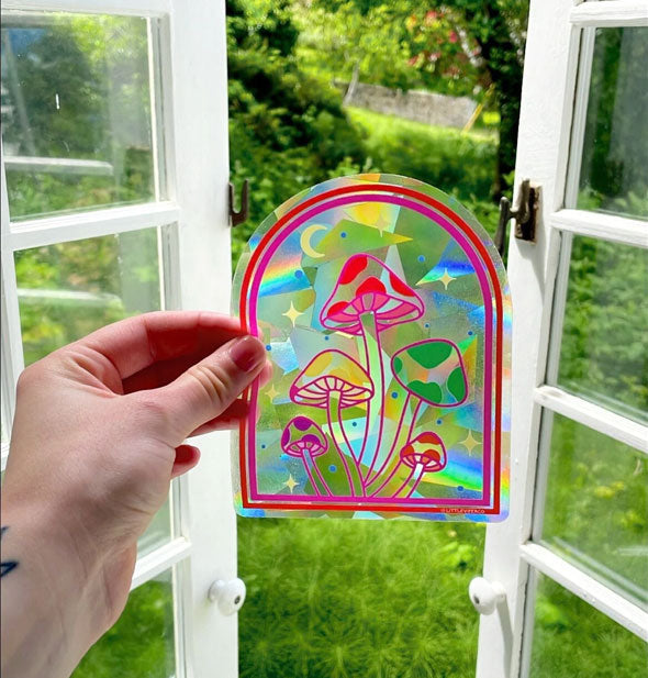 Model's hand holds a rainbow-effect mushrooms decal in front of an opened window