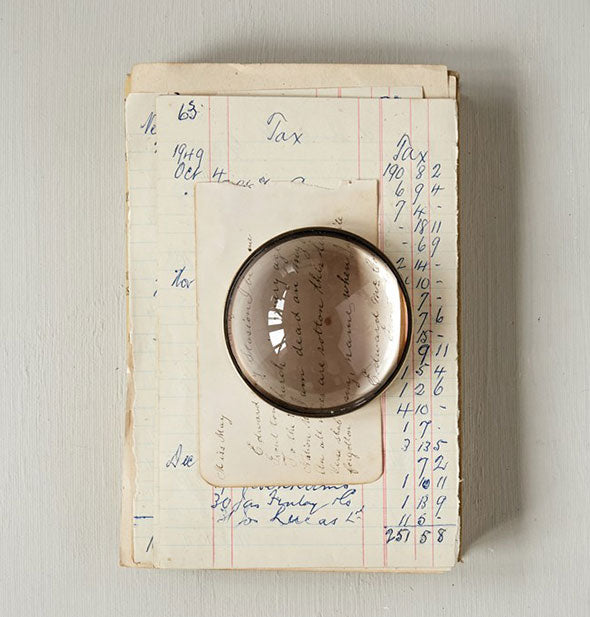 Round magnifying glass sits on top of a vintage ledger