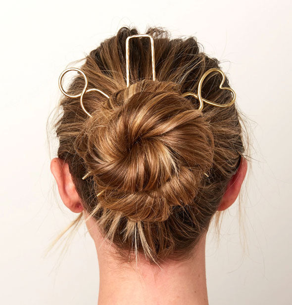 Model wears circular, rectangular, and heart-shaped brass hair picks in a twisted updo