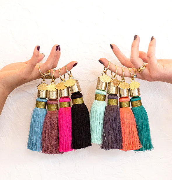 Two models' hands hold colorful tassel keychains on their fingers