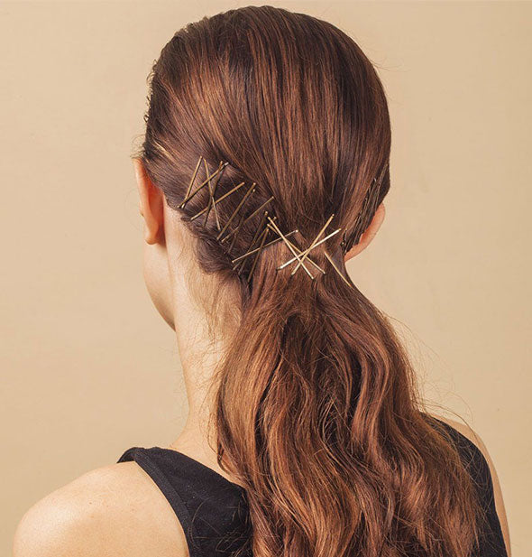Model wears a number of gold bobby pins in a low ponytail
