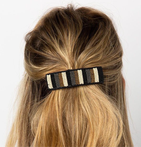 Model wears a rectangular striped beaded barrette in a swept-back hairstyle