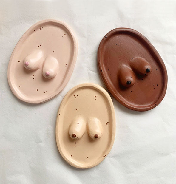 Pink, tan, and brown oval-shaped ceramic trays each with a pair of raised breasts