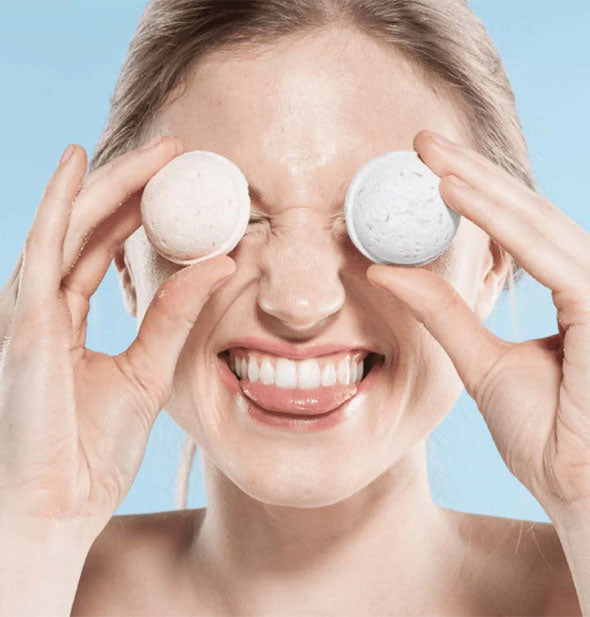 Smiling model holds two small bath bombs in front of eyes