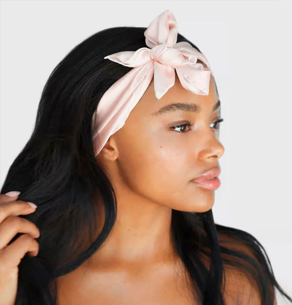 Model wears a pink satin sleep scarf as a headband tied in a bow in front