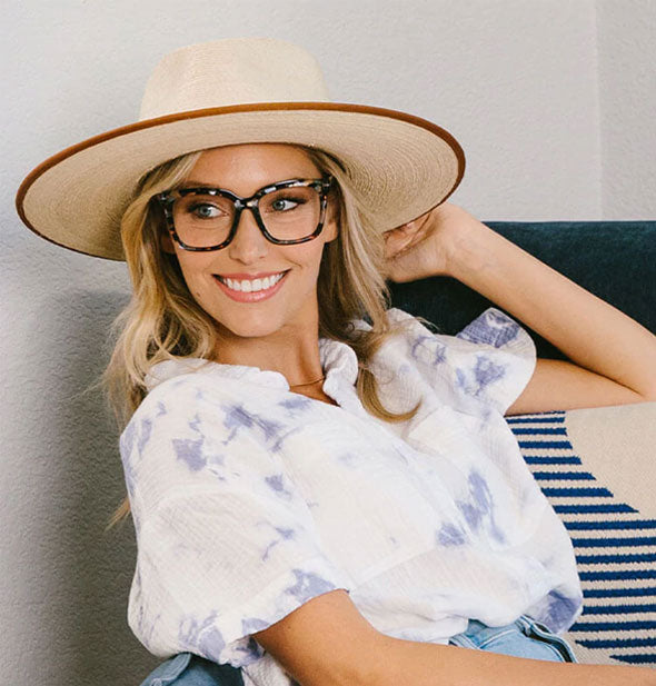 Smiling model in a wide-brimmed hat wears an oversized square-shaped pair of blue and brown flecked glasses