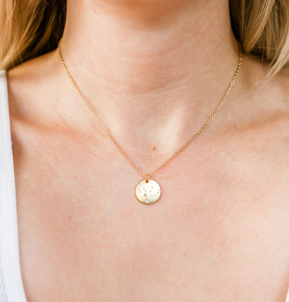 Model wears a gold zodiac sign necklace with round stamped pendant