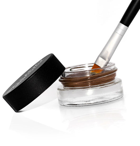 A brush dips into a pot of Palladio Brow Pomade