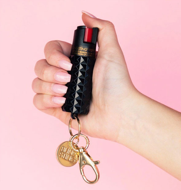 Model's hand holds a black Blingsting pepper spray canister