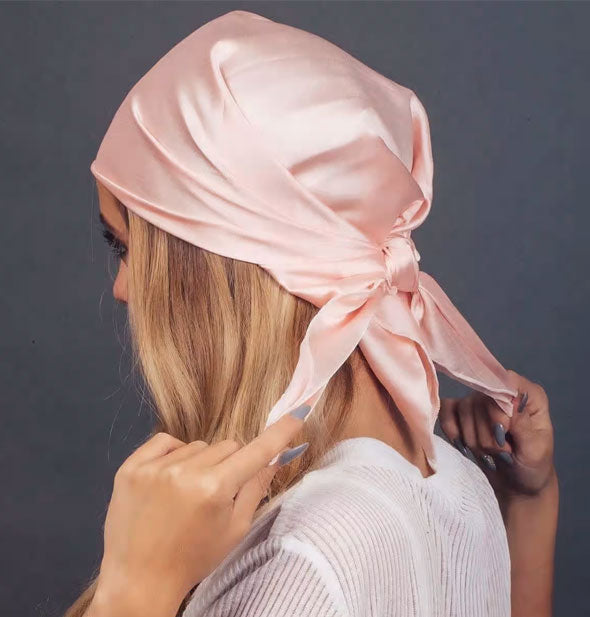 Model ties a pink satin sleep scarf in back of head
