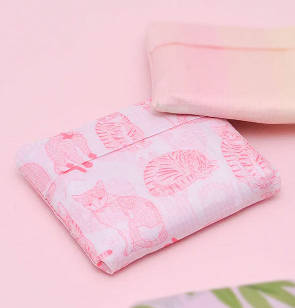 A folded up pink cat print tote bag forms a tidy parcel; two others are partially shown in the background and foreground