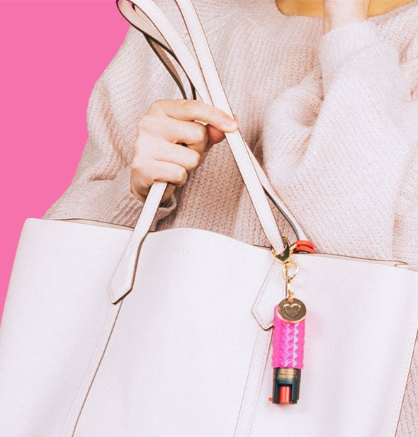 Model poses with pink Blingsting pepper spray canister attached to purse handle