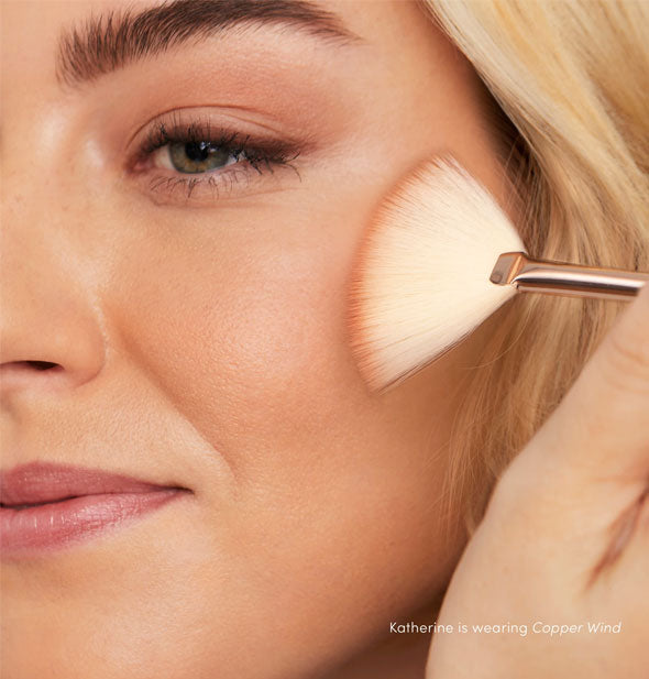 Model applies PurePressed Blush to cheek in the shade Copper Wind with a white fan brush