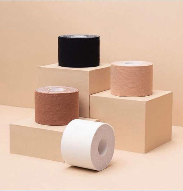Four rolls of breast tape in different flesh tones on block platforms