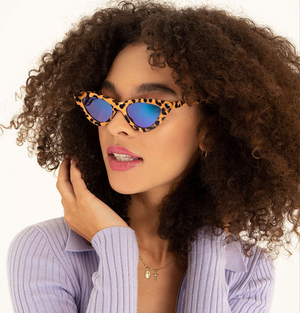 Model wears a cheetah print pair of cat-eye sunglasses with a reflective blue lens