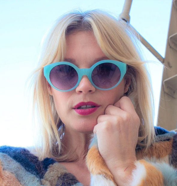 Model wears a blue pair of round sunglasses with dark purple lens
