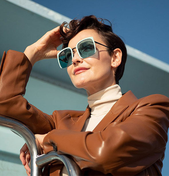 A model with arm raised wears a pair of three-quarter frame sunglasses in direct sunlight