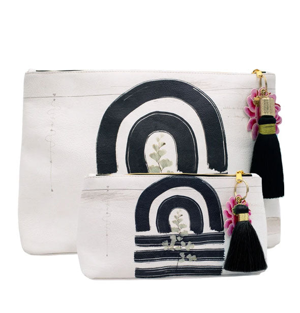 Small and large white pouches with black brushstroke design and black tassels attached to gold zipper hardware