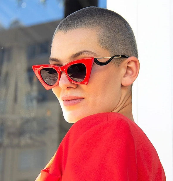 Model wears a pair of angular red sunglasses with a curved arm