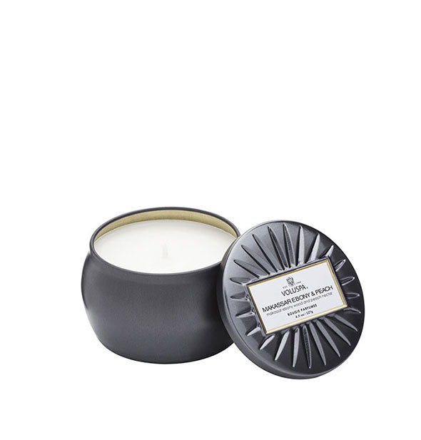 Metallic black Makassar Ebony & Peach Voluspa tin candle with lid featuring radial embossing set to the side