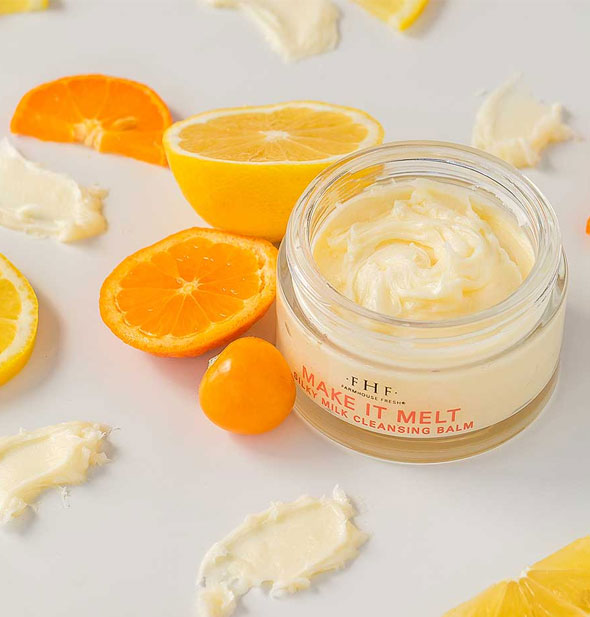 Opened pot of FarmHouse Fresh Make It Melt Silky Milk Cleansing Balm with smeared product samples and orange fruit surrounding it