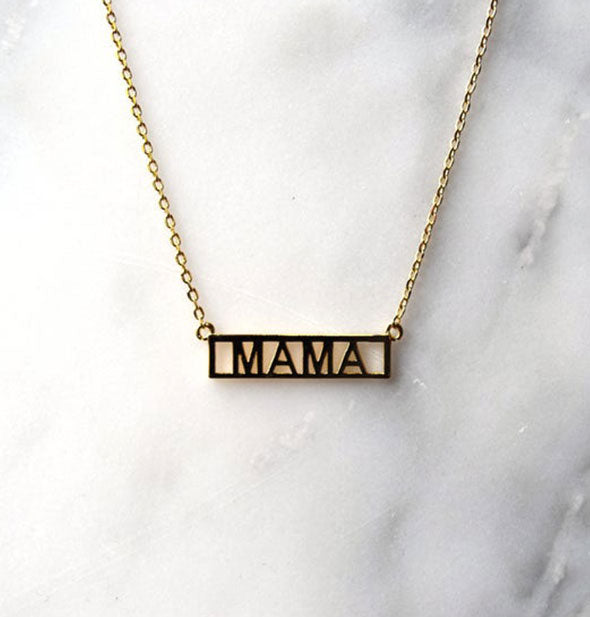 Gold bar necklace on white marble surface says, "Mama"
