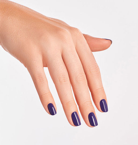 Model's hand wears a dark purple shade of nail polish