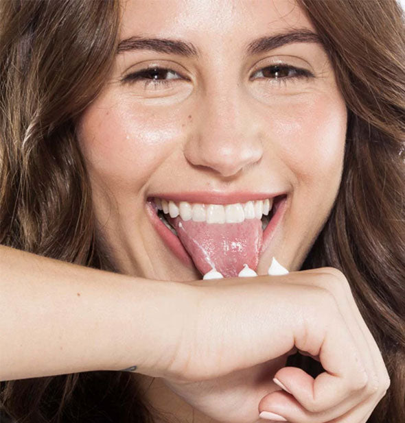 Model playfully pretends to lick small dollops of hand cream on the back of her hand