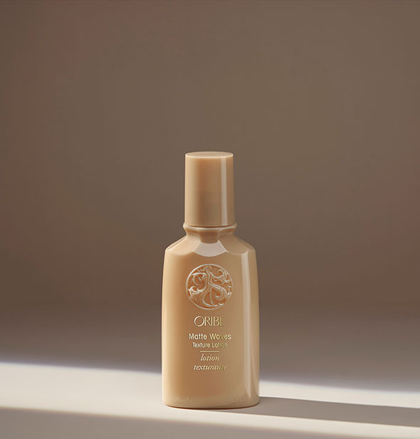 Small gold bottle of Oribe Matte Waves Texture Lotion on a neutral background
