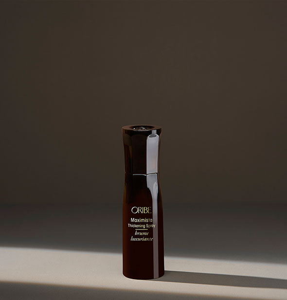 Small brown bottle of Oribe Maximista Thickening Spray on a dark background