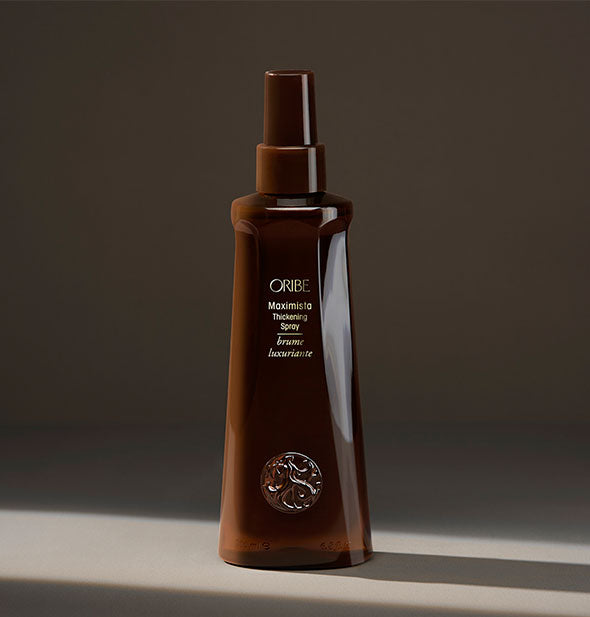 Brown bottle of Oribe Maximista Thickening Spray on a dark background