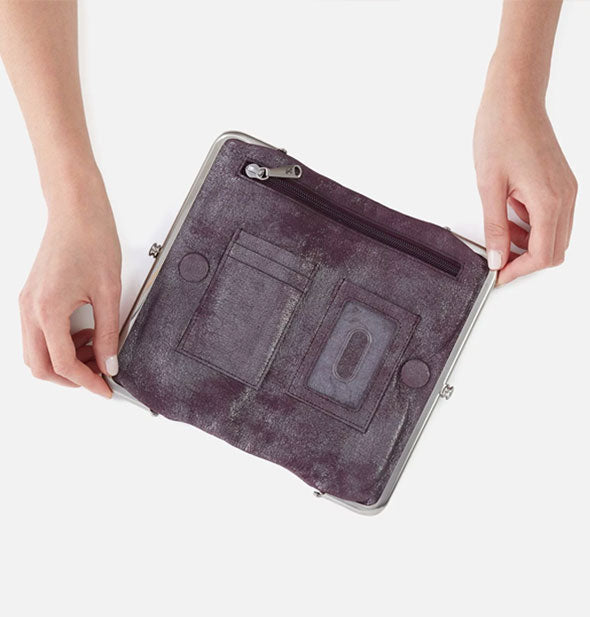 Model's hands hold open a Hobo wallet to reveal card slots and zipper pocket inside