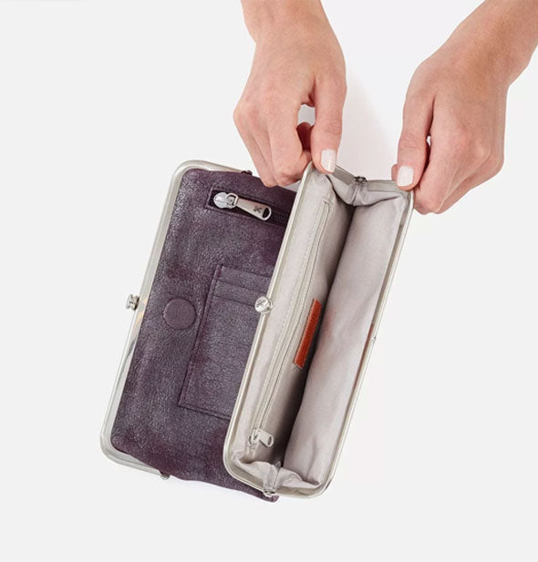 Model's hands hold open a frame compartment of a Hobo wallet to show storage inside