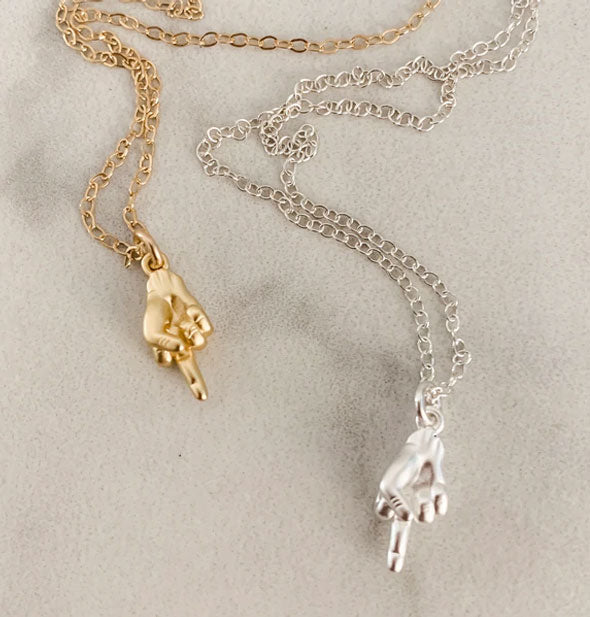 Two middle finger hand pendant necklaces, one in a gold finish and one in a silver finish