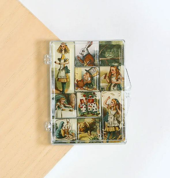 Set of 10 magnets depicting illustrated scenes from Alice in Wonderland in clear jewel case on white and wood surface