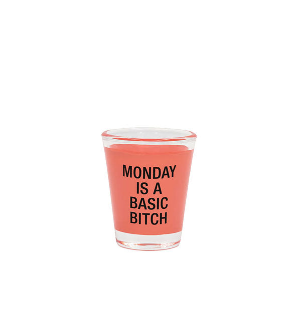Clear shot glass with salmon-colored band says, "Monday is a basic bitch" in black lettering
