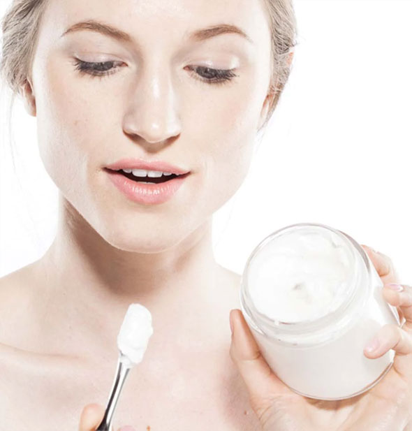 Model holds a jar of moisturizer and an applicator with some product on the end
