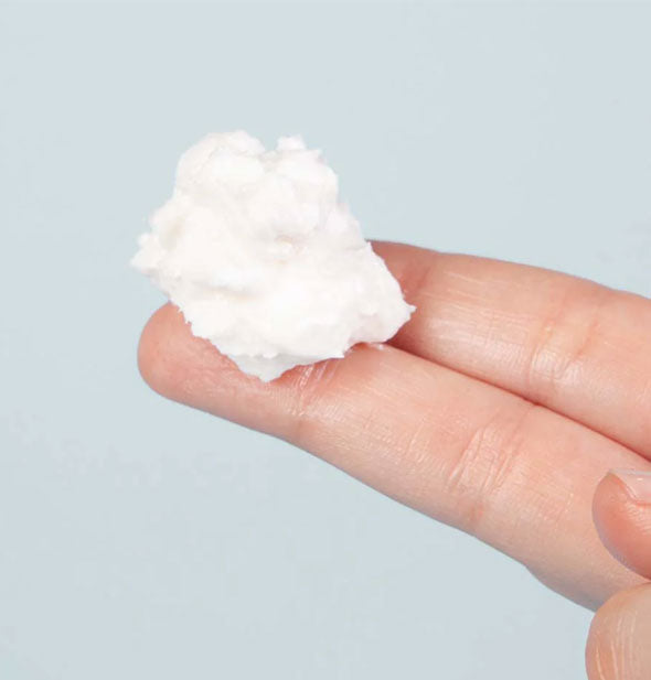 Model's fingers hold a glob of white, fluffy moisturizer