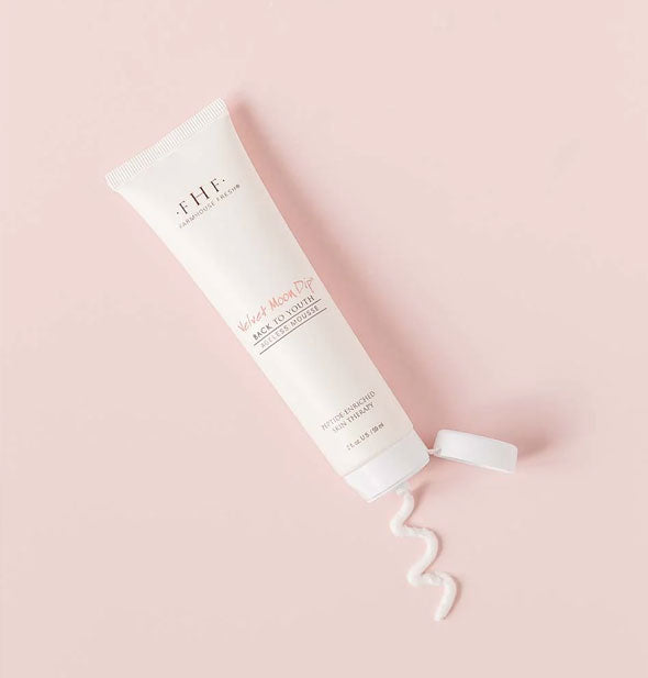A tube of FarmHouse Fresh Velvet Moon Dip Back to Youth Ageless Mousse squirts out a squiggle of product onto a pink surface