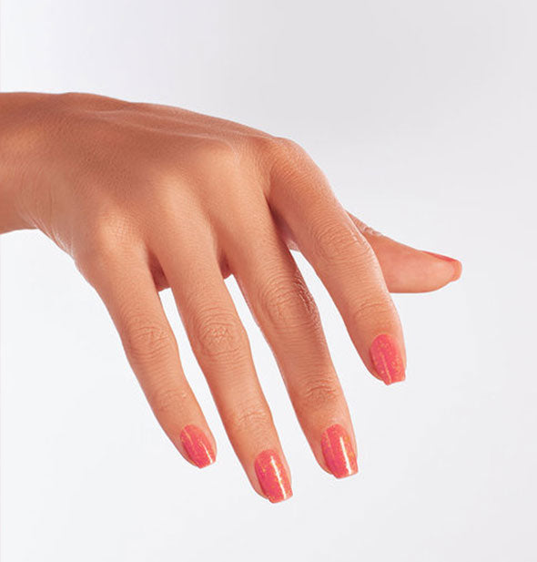 Model's hand wears a glittery coral shade of nail polish