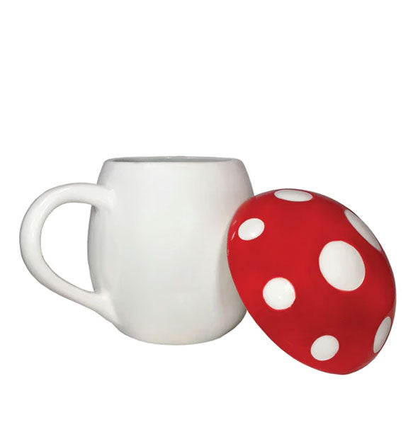 Rounded white mug with red and white spotted mushroom cap lid set to the side