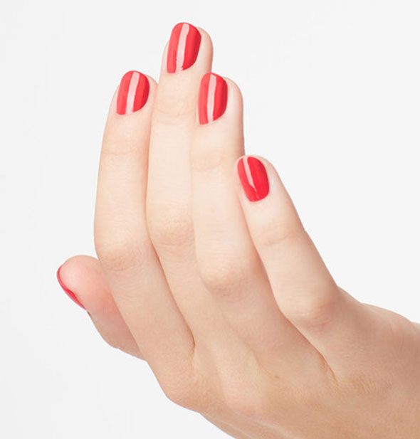 Model's hand wears a bright coral shade of nail polish
