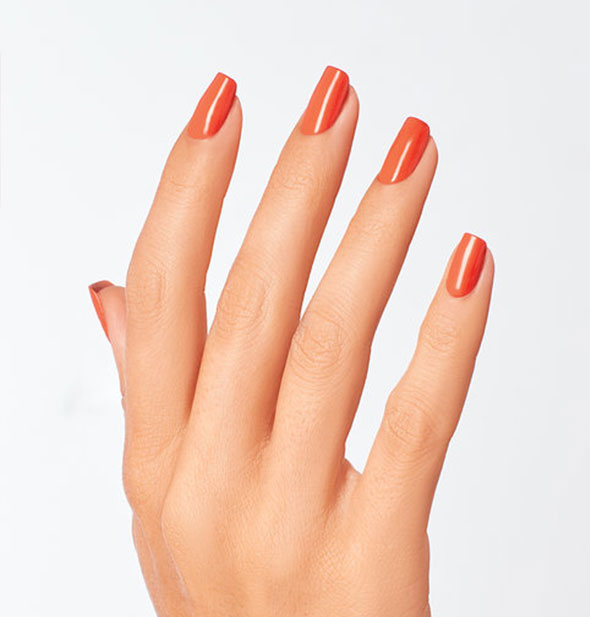 Model's hand wears an orange shade of nail polish