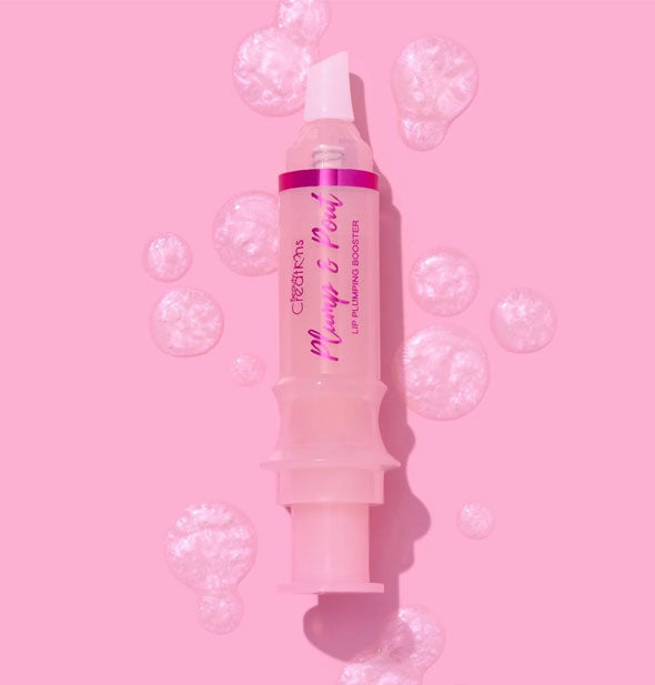 A syringe-shaped tube of Beauty Creations Plump & Pout lip gloss surrounded by light iridescent droplets of product